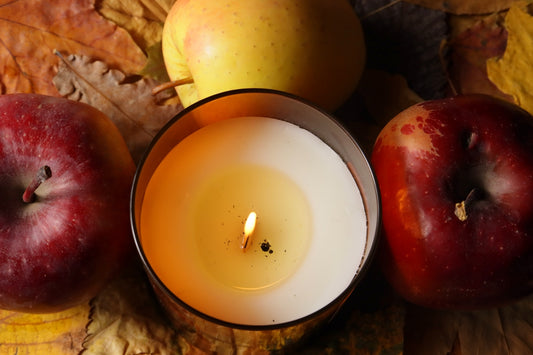 Three apples and a lit candle on autumn leaves.