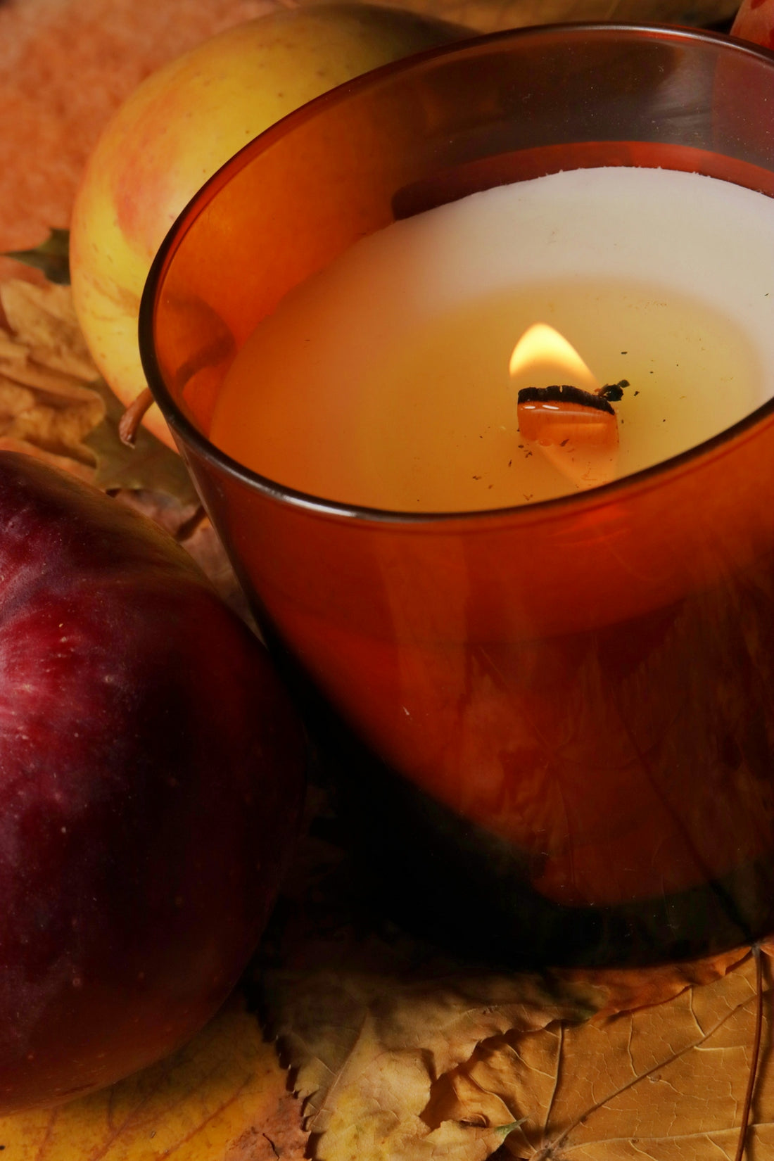 A lit candle with apples and autumn leaves