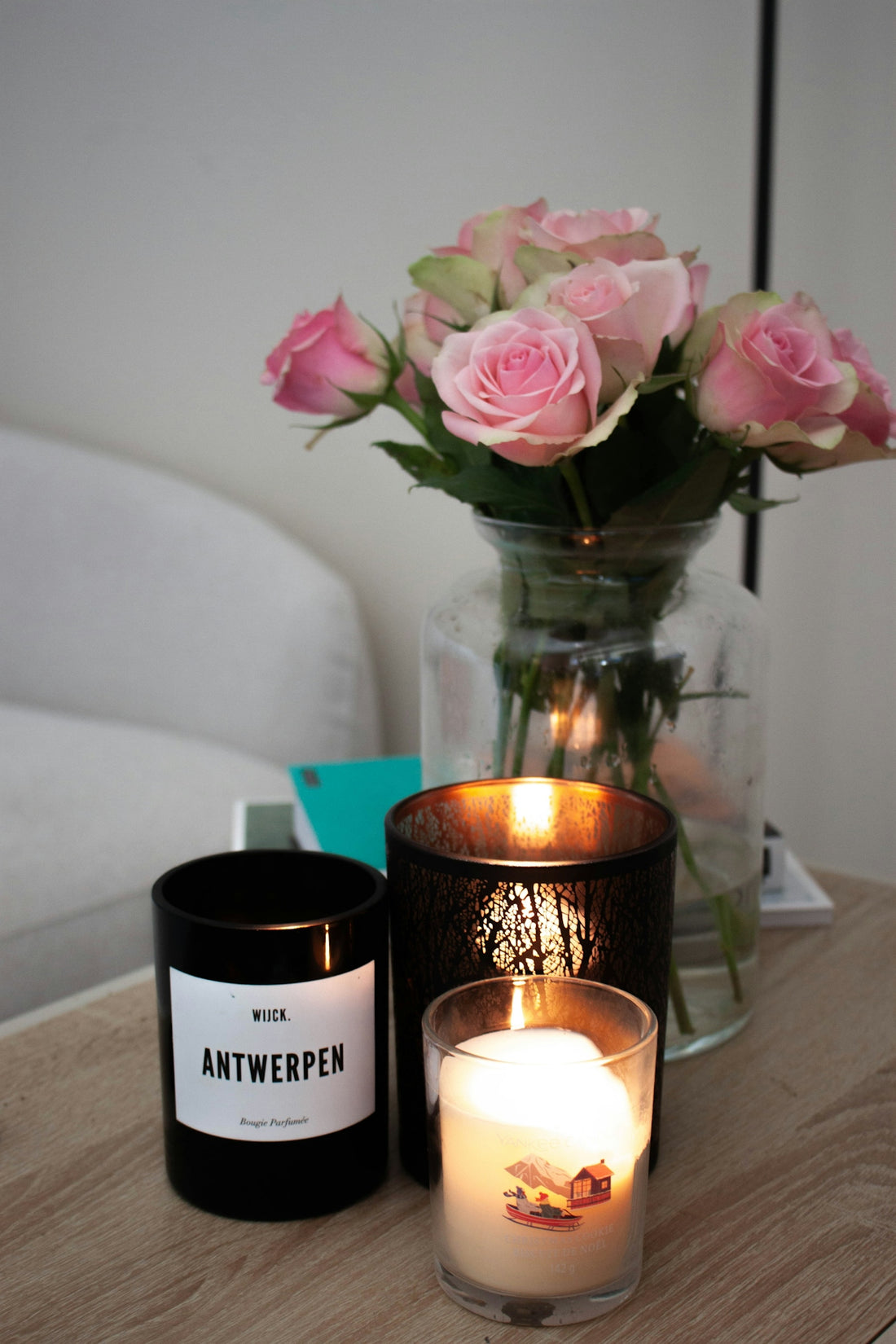 Three lit candles and pink roses in vase.