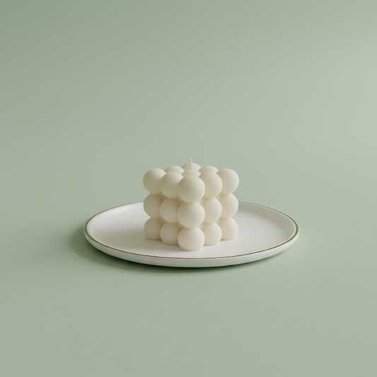 A white bubble candle sits on a white plate with a gold rim.