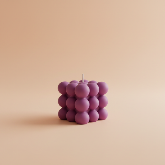 A purple bubble candle with a white wick on a peach background.