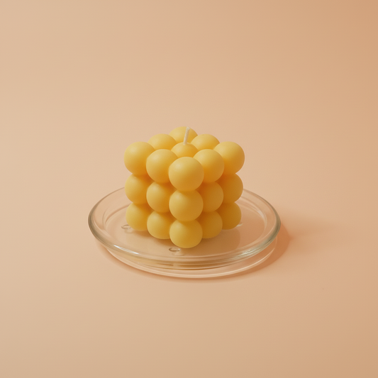 A yellow bubble-shaped candle sits on a clear glass tray against a peach-colored background.
